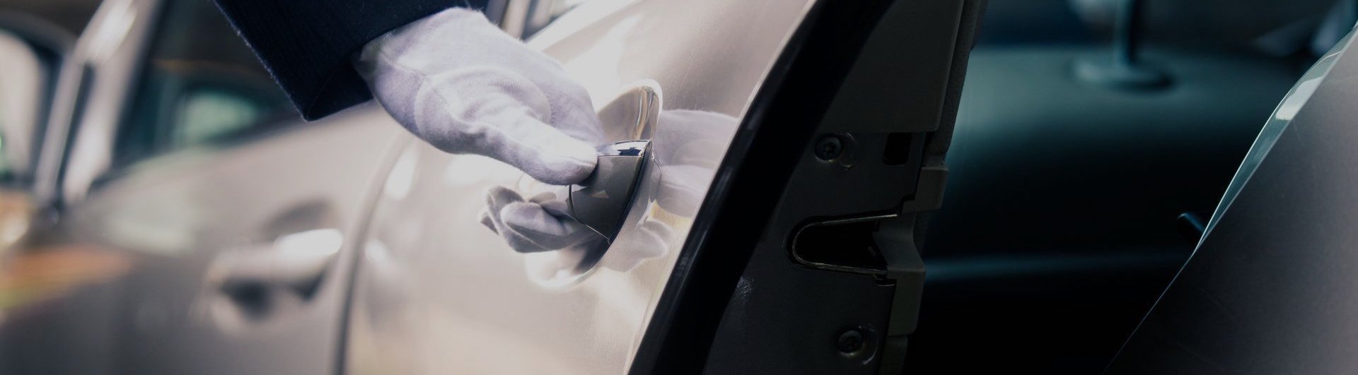 A gloved hand opens a car door from the outside, showing part of the vehicle's interior and side mirror.