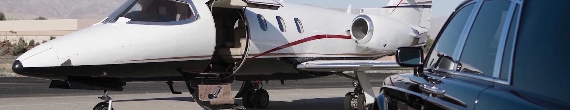 Private jet on a tarmac with its door open, parked next to a black luxury car under a clear sky.