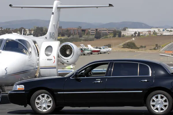 A private jet parked on a tarmac beside a black luxury car.