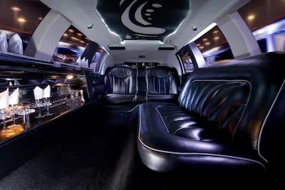Elegant limo interior with plush black leather seating, ambient lighting, and a stocked bar on the side.